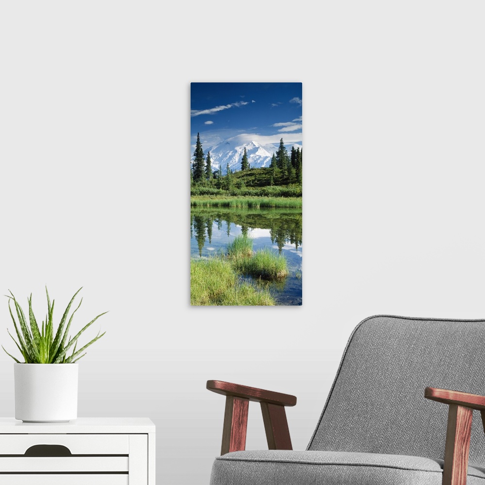 A modern room featuring This is a vertical photograph of a mountain peak, trees, and clouds reflecting in a pond in an Al...