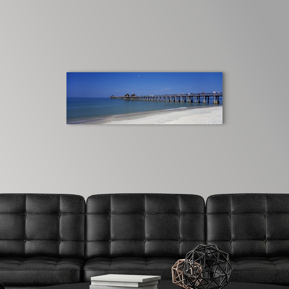 A modern room featuring This wall art is a panoramic photograph of a beach board walk extending into the ocean.