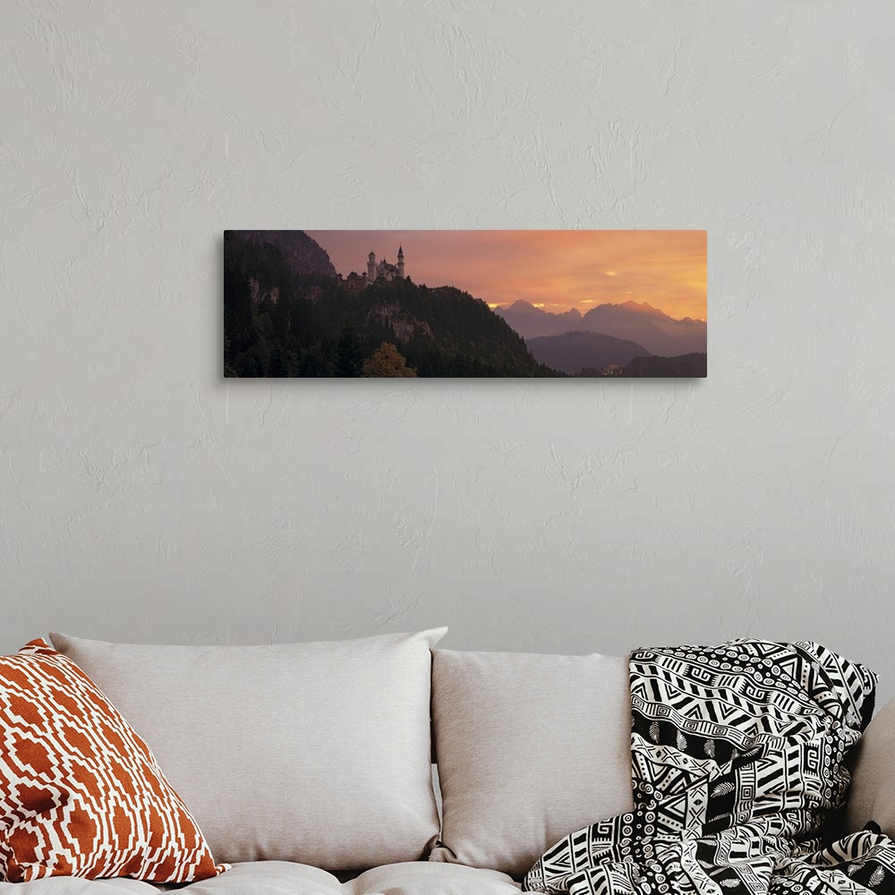 A bohemian room featuring A large panoramic piece of a castle sitting in the mountains in Germany. The sky has warm tones a...