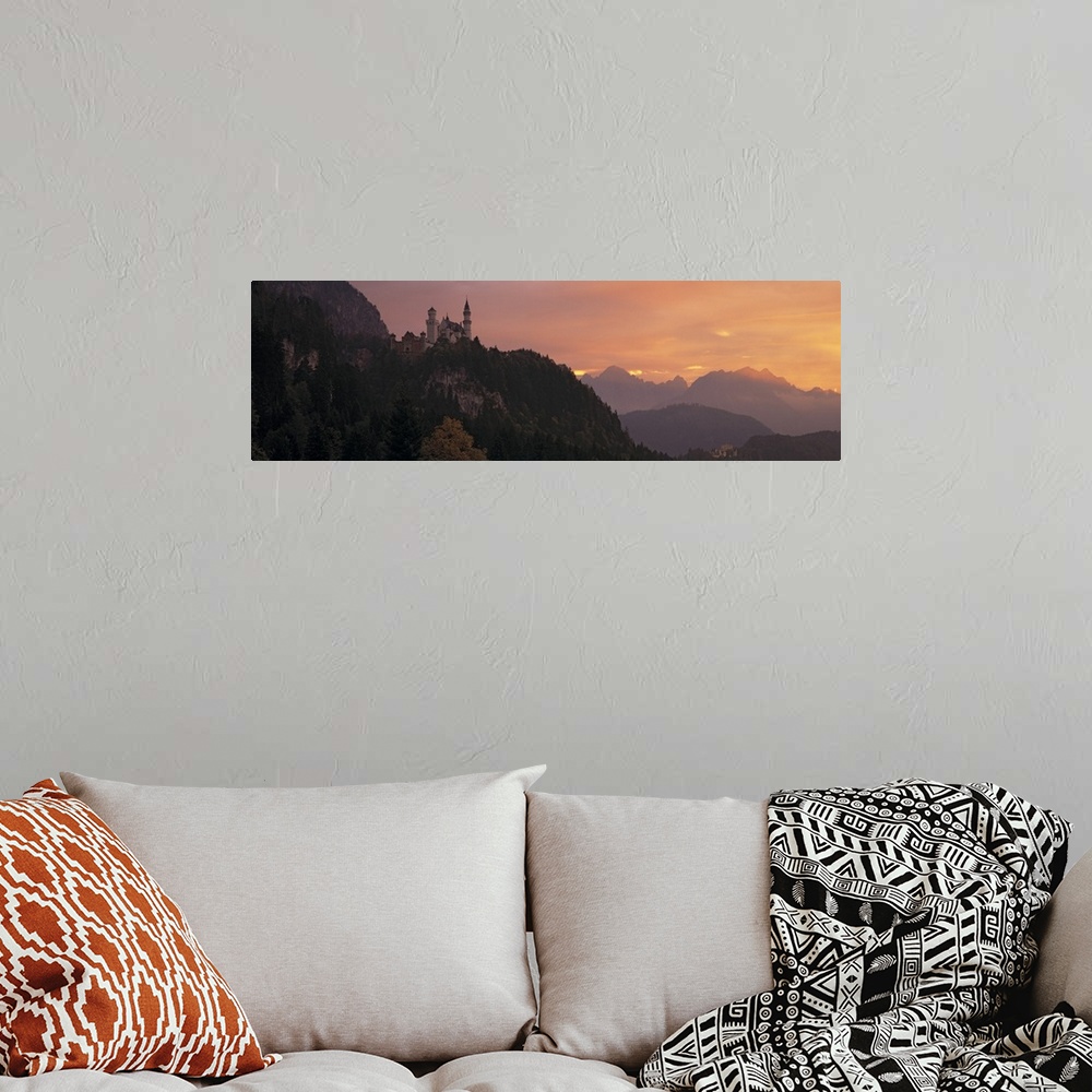 A bohemian room featuring A large panoramic piece of a castle sitting in the mountains in Germany. The sky has warm tones a...