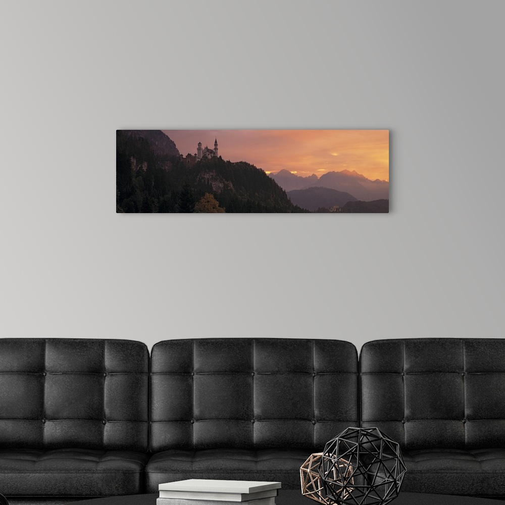 A modern room featuring A large panoramic piece of a castle sitting in the mountains in Germany. The sky has warm tones a...