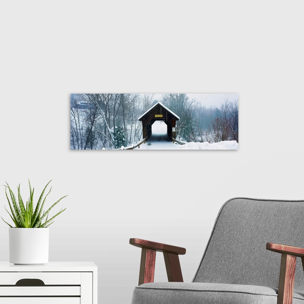 A modern room featuring A panoramic photograph of a one lane road through a covered bridge in a winter snowscape.
