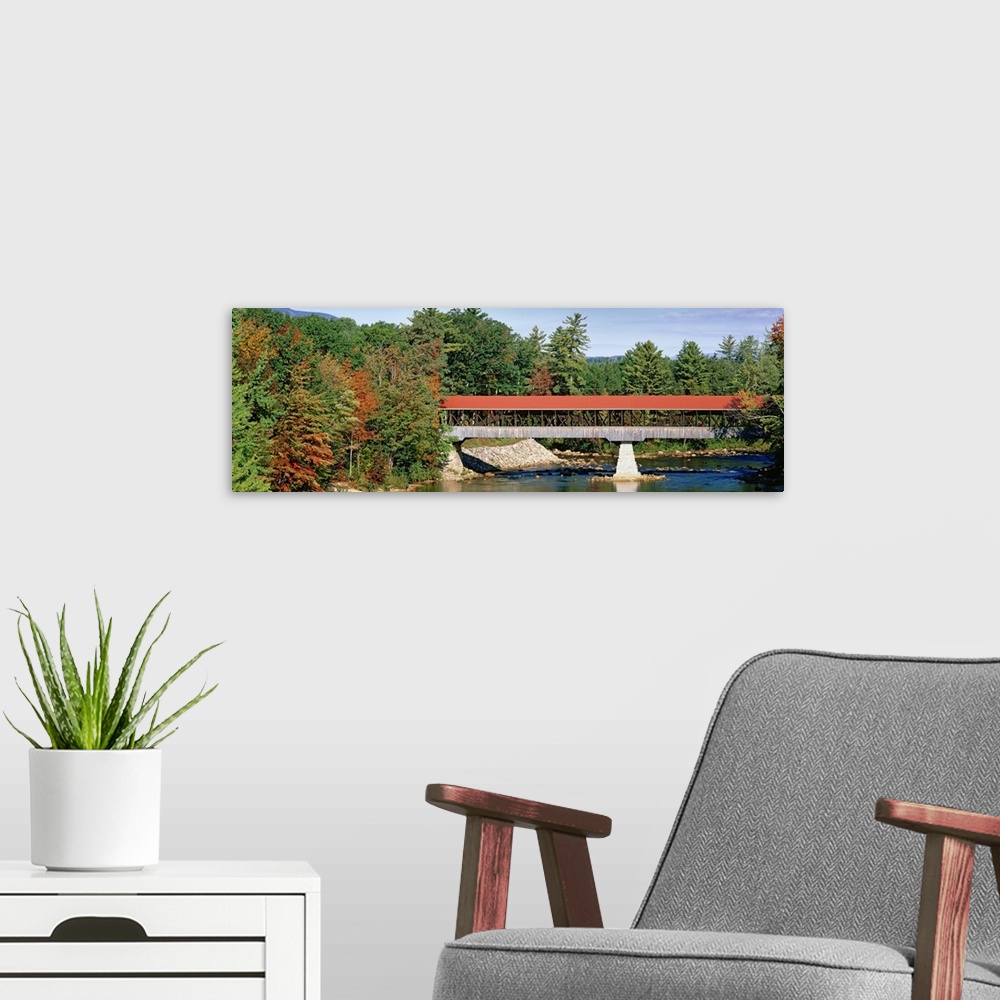 A modern room featuring Panoramic image of a red roofed covered bridge spanning a calm tree lined river.