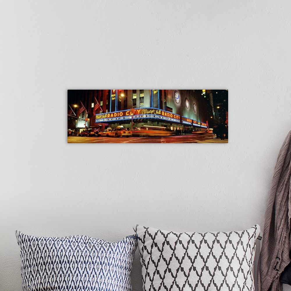 A bohemian room featuring Panoramic view of Radio City Music Hall from the street corner at night, lit up by neon lights an...