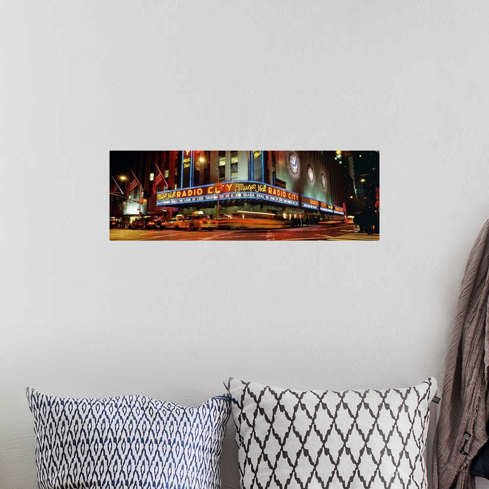 A bohemian room featuring Panoramic view of Radio City Music Hall from the street corner at night, lit up by neon lights an...