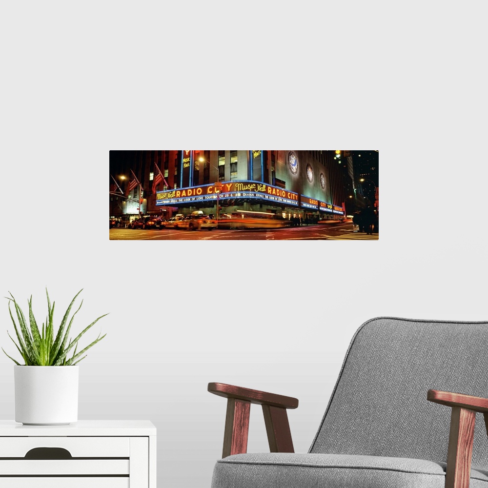 A modern room featuring Panoramic view of Radio City Music Hall from the street corner at night, lit up by neon lights an...