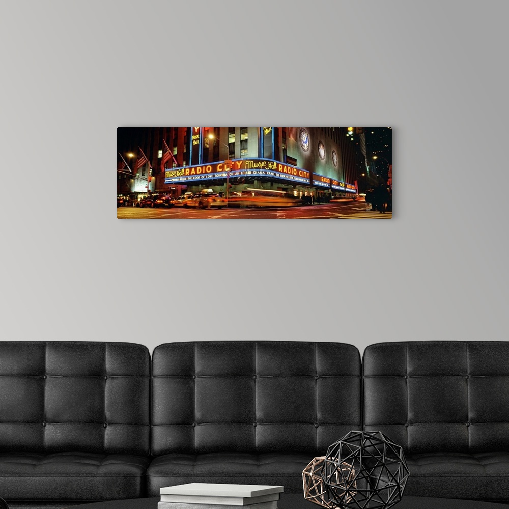 A modern room featuring Panoramic view of Radio City Music Hall from the street corner at night, lit up by neon lights an...