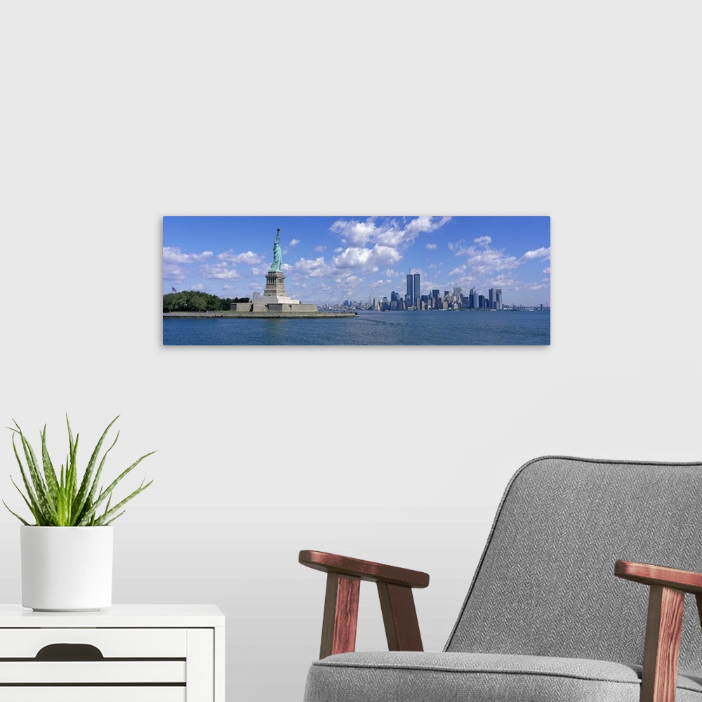 A modern room featuring Panoramic picture taken from a distance of the NYC skyline with Ellis Island and the Statue of Li...