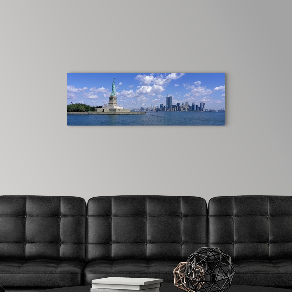 A modern room featuring Panoramic picture taken from a distance of the NYC skyline with Ellis Island and the Statue of Li...