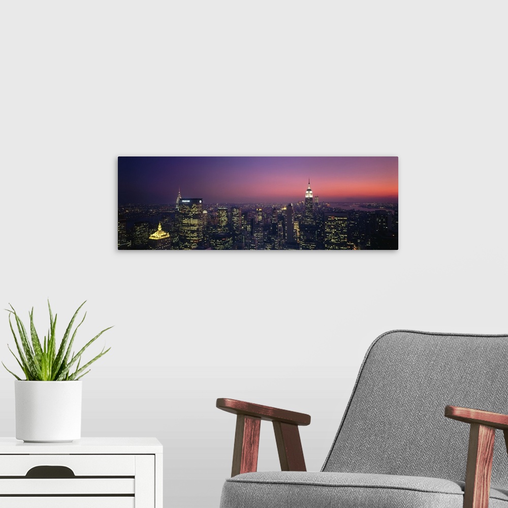 A modern room featuring Aerial view of New York City at late dusk with lit up office buildings, the Chrysler Building, an...