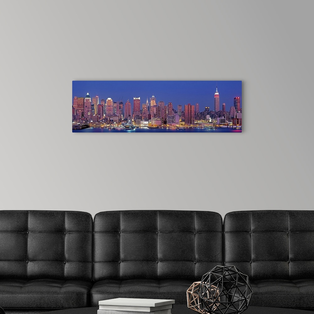 A modern room featuring Wide angle photograph of the West side of the New York City skyline, lit up at night, against a d...