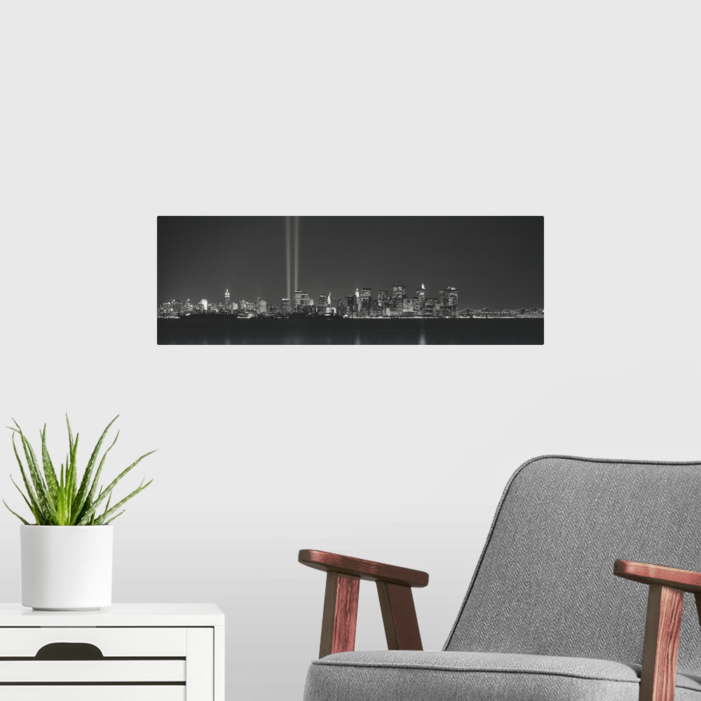 A modern room featuring Panoramic vista of the New York City skyline in the evening, with beams of light from the World T...