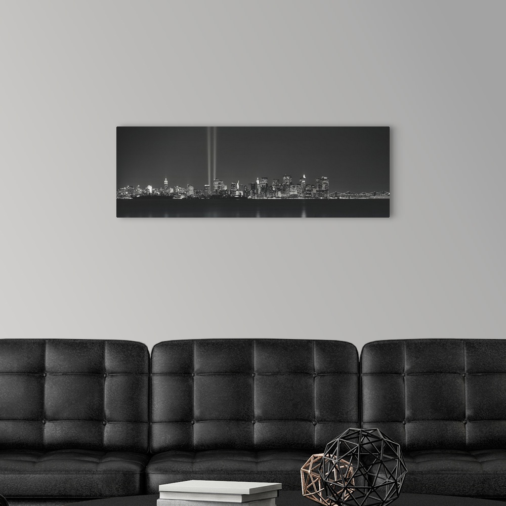 A modern room featuring Panoramic vista of the New York City skyline in the evening, with beams of light from the World T...