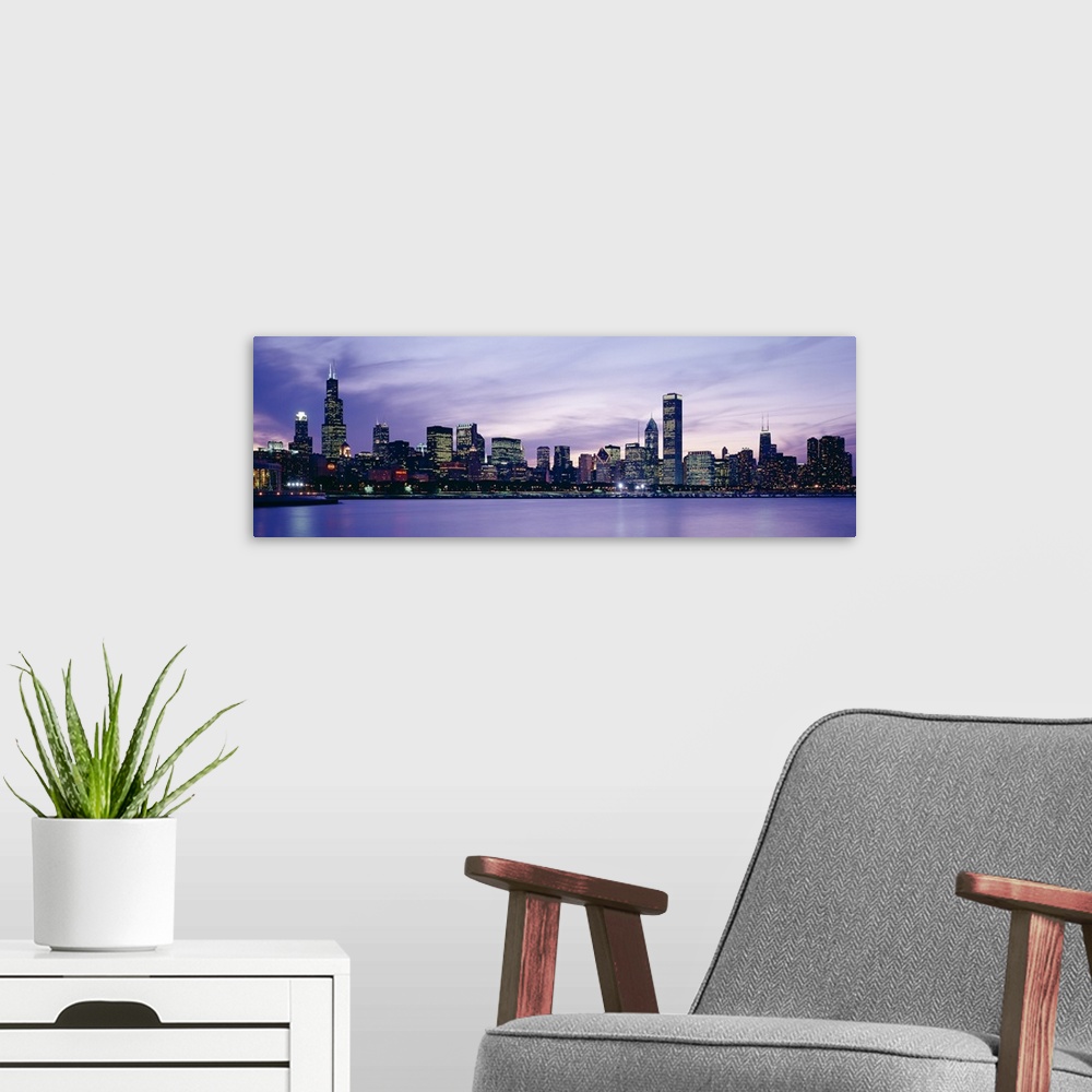 A modern room featuring Big canvas photo of an illuminated cityscape along a smooth waterfront at dusk.