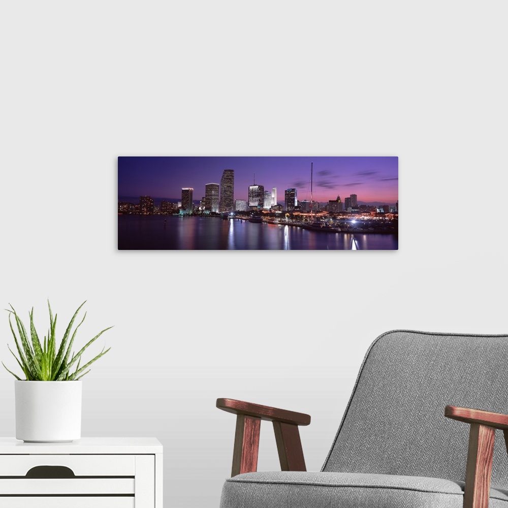 A modern room featuring This wall art shows the city skyline reflecting in the water of a panoramic photograph for the ho...