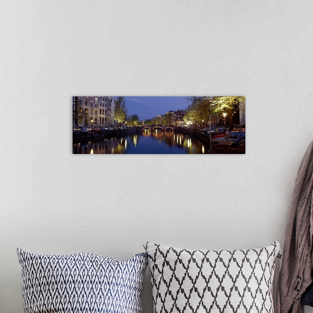 A bohemian room featuring A wide angle view of a canal in Amsterdam with buildings and street lights illuminated on either ...