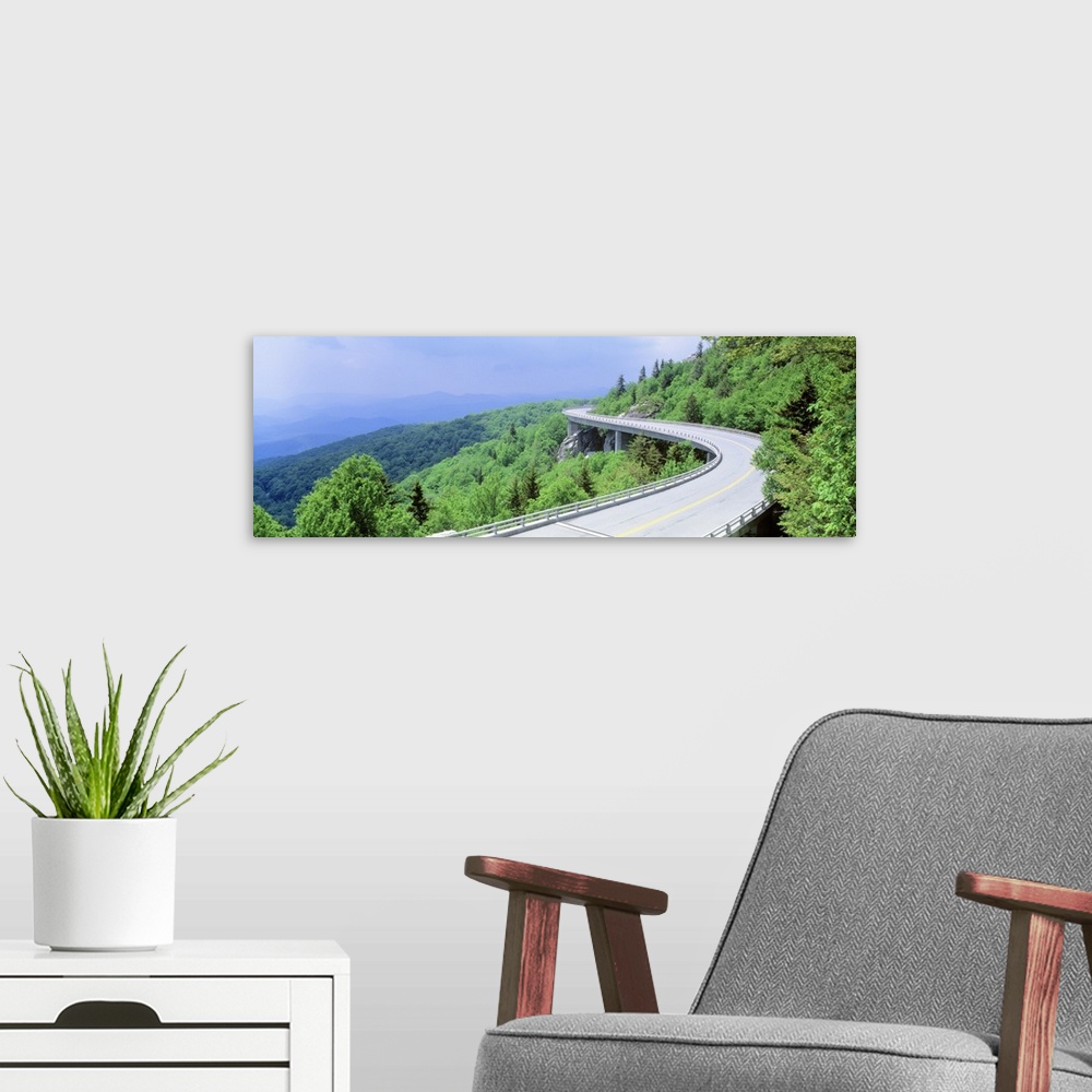 A modern room featuring Panoramic photograph of road winding through tree covered mountains.