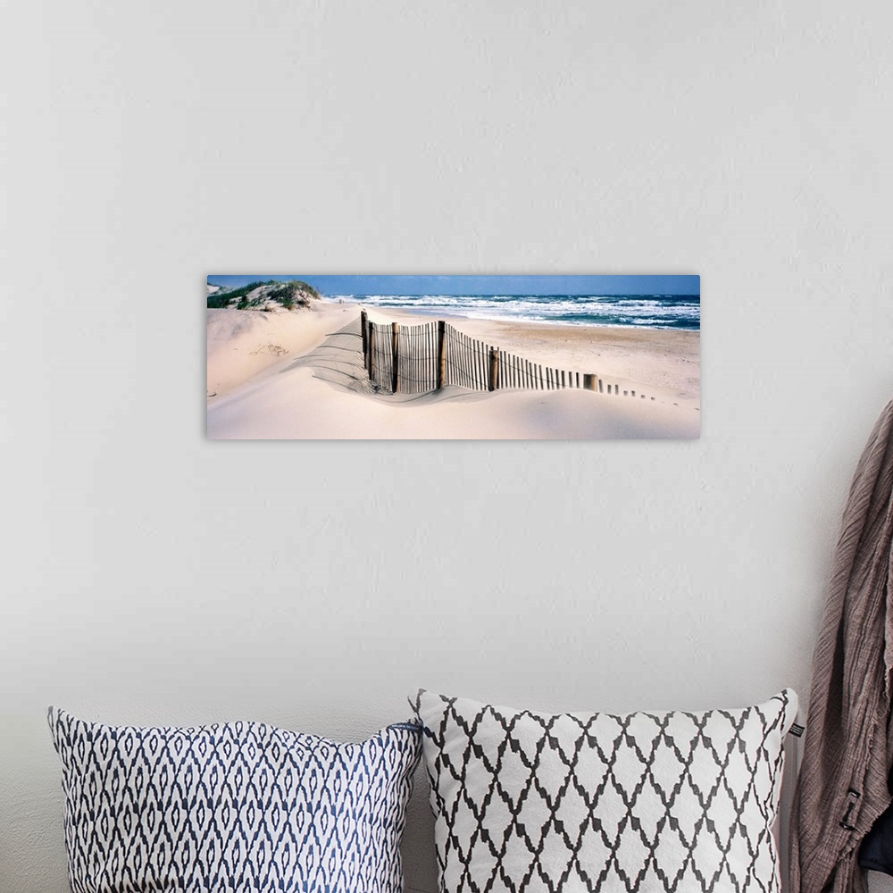 A bohemian room featuring A wooden fence separates sand dunes from the Atlantic Ocean in this panoramic image.