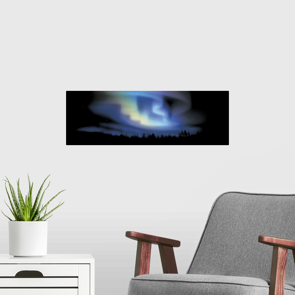 A modern room featuring This large panoramic picture is taken of the northern lights with the sky and land below blacked ...