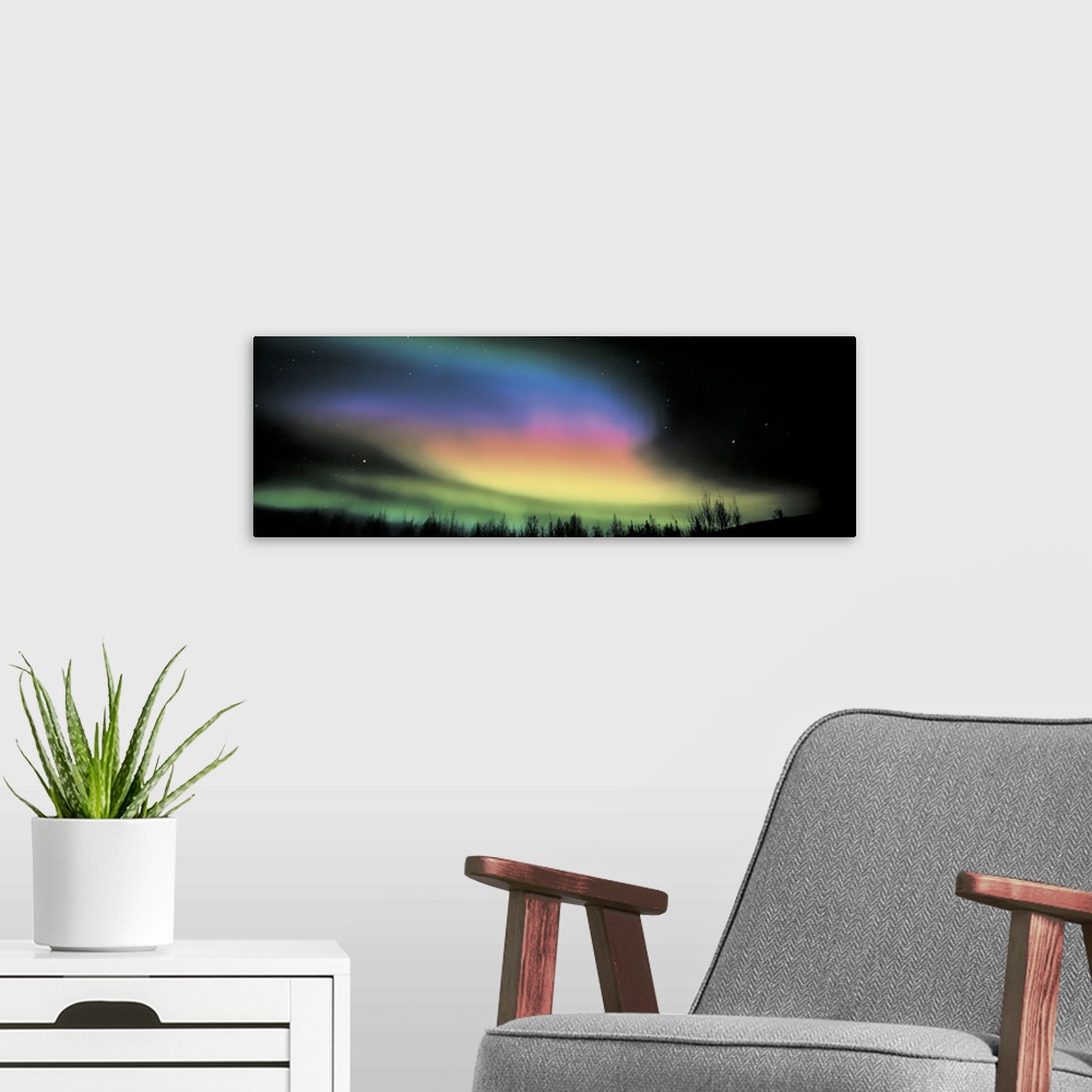 A modern room featuring Panoramic photograph taken of the northern lights. Swirls of color brighten the dark night sky.