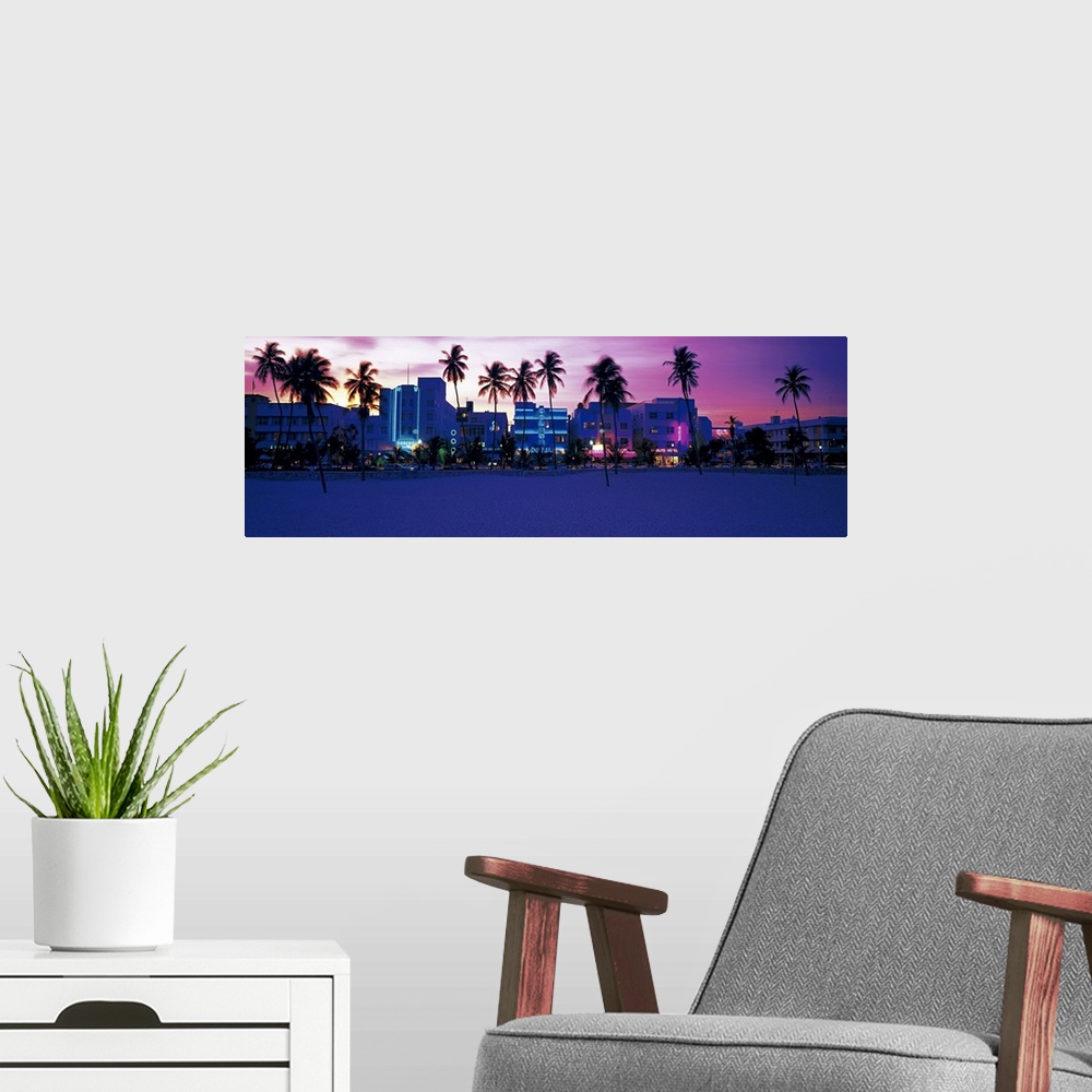 A modern room featuring Oversized, landscape photograph of palm trees along Miami Beach, the lit buildings along Ocean Dr...