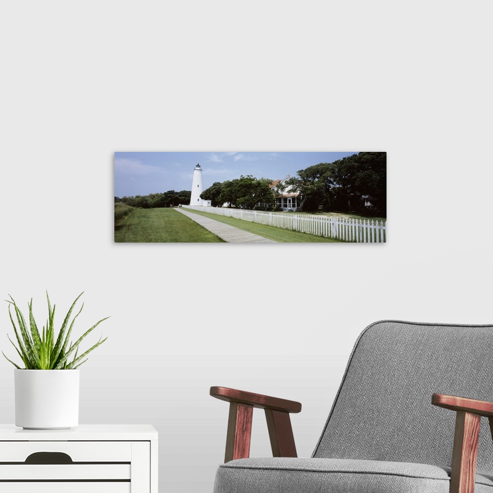 A modern room featuring Horizontal photograph on a big canvas of a thin boardwalk and fence leading to a lighthouse surro...