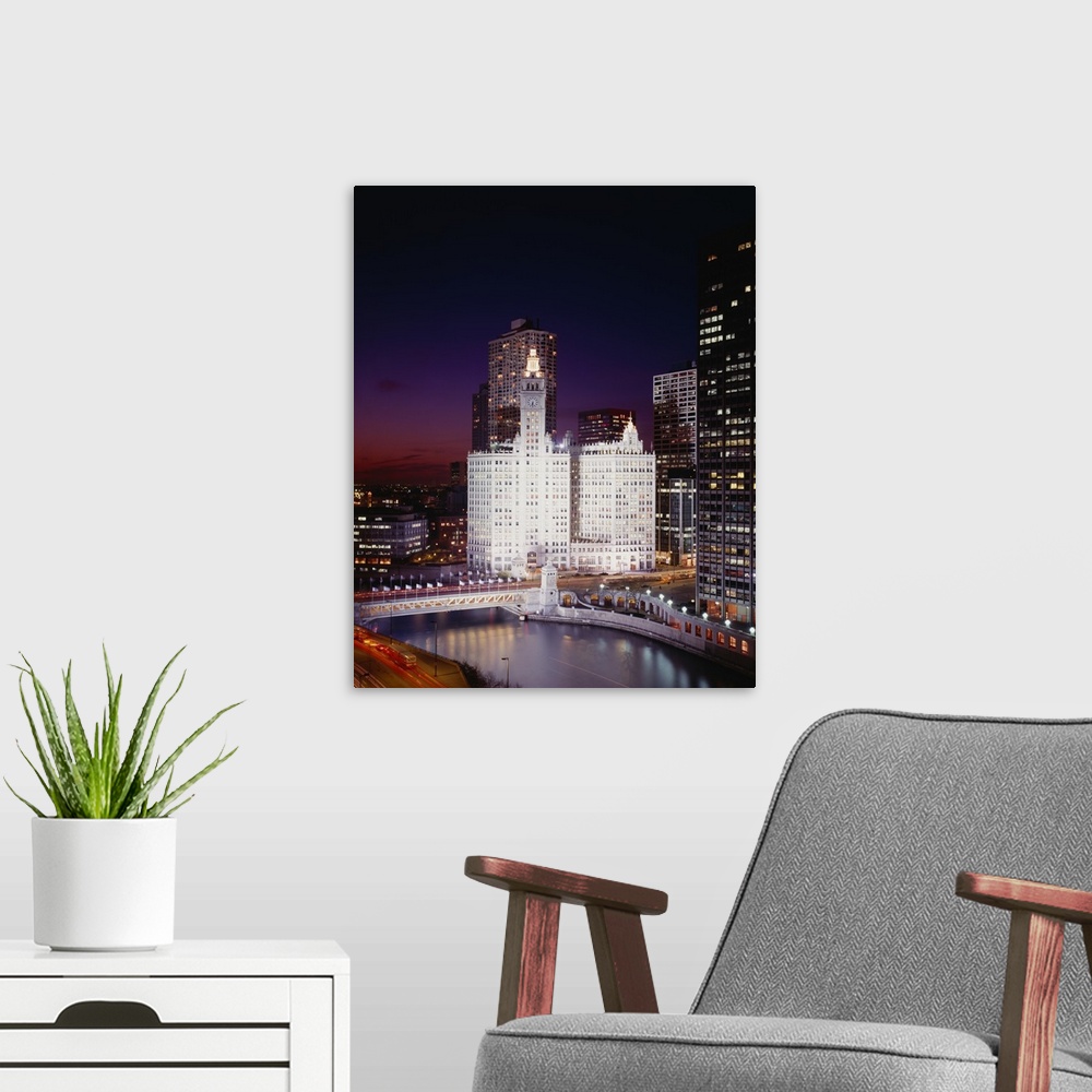 A modern room featuring A view of buildings in Chicago at night with the windows illuminated. A bridge and body of water ...