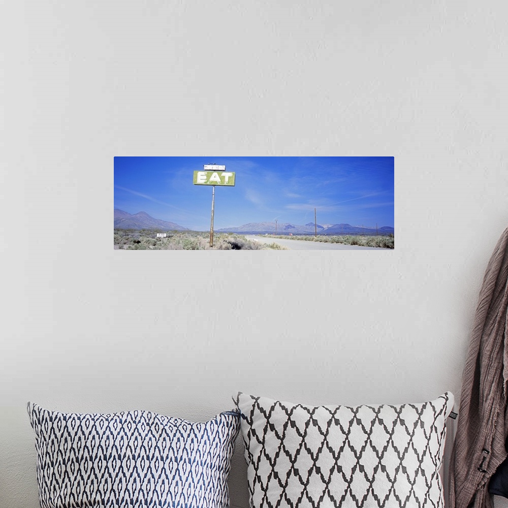 A bohemian room featuring A large sign with the word Eat stands alone in the desert with mountainous terrain lining the bac...
