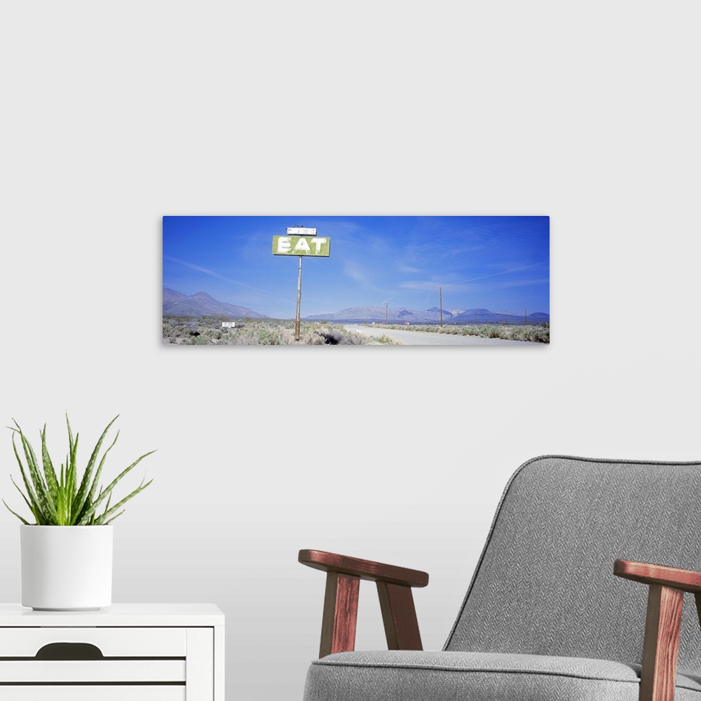 A modern room featuring A large sign with the word Eat stands alone in the desert with mountainous terrain lining the bac...