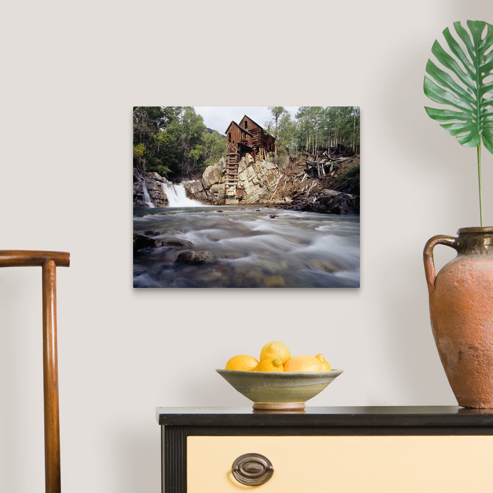 A traditional room featuring Photograph of old log cabin sitting on top of rocky hill with rushing stream below.