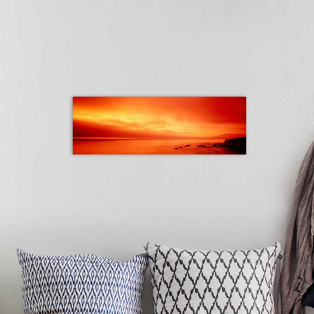 A bohemian room featuring Panoramic photograph displays the vibrant glow of the sun shining over a coastline within the Wes...