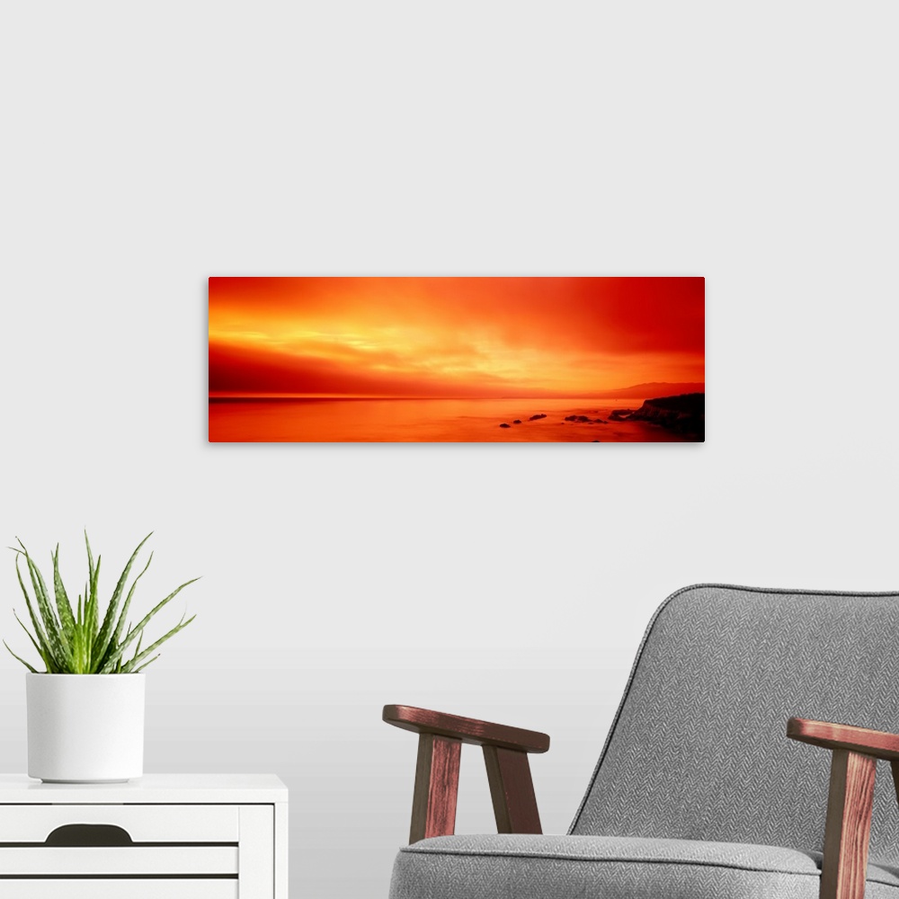 A modern room featuring Panoramic photograph displays the vibrant glow of the sun shining over a coastline within the Wes...
