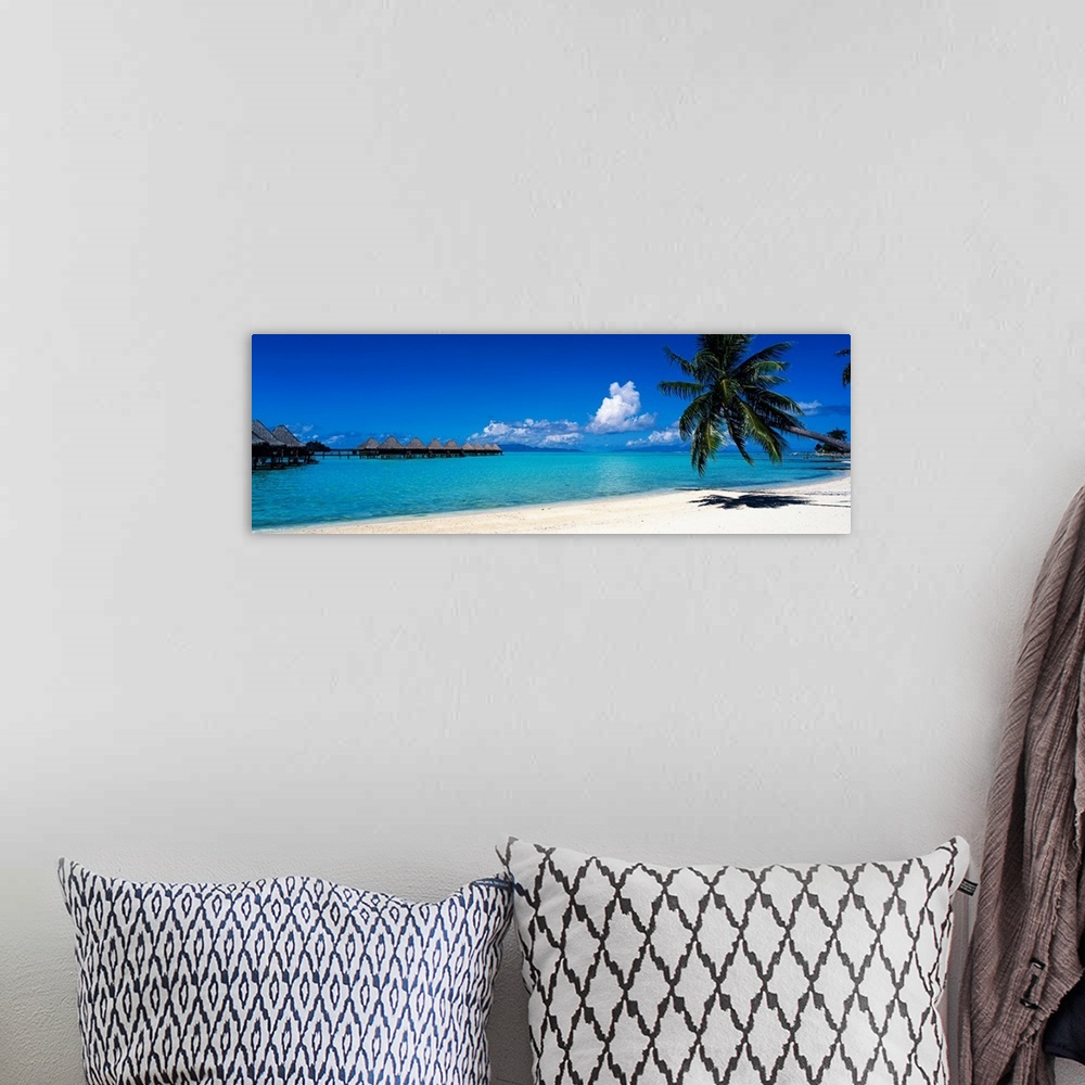 A bohemian room featuring A panoramic photograph of a tropical beach with palm trees and thatch huts over the water.