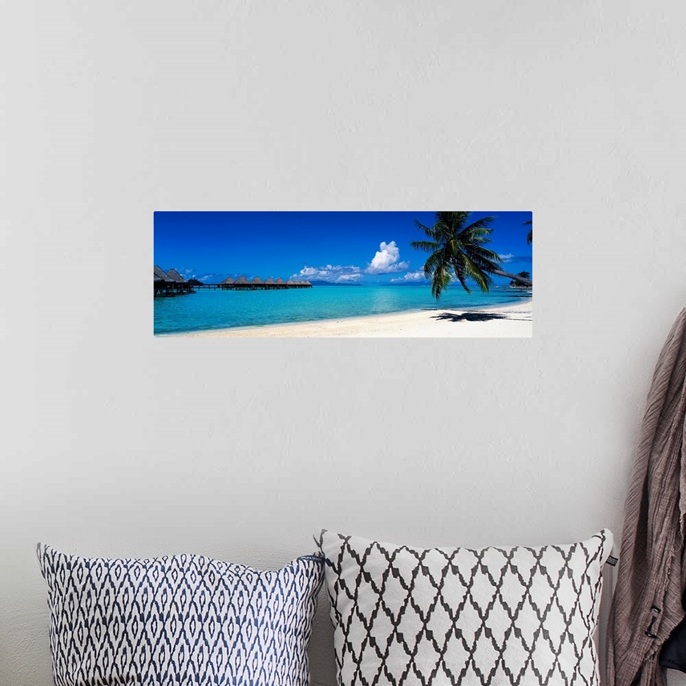 A bohemian room featuring A panoramic photograph of a tropical beach with palm trees and thatch huts over the water.