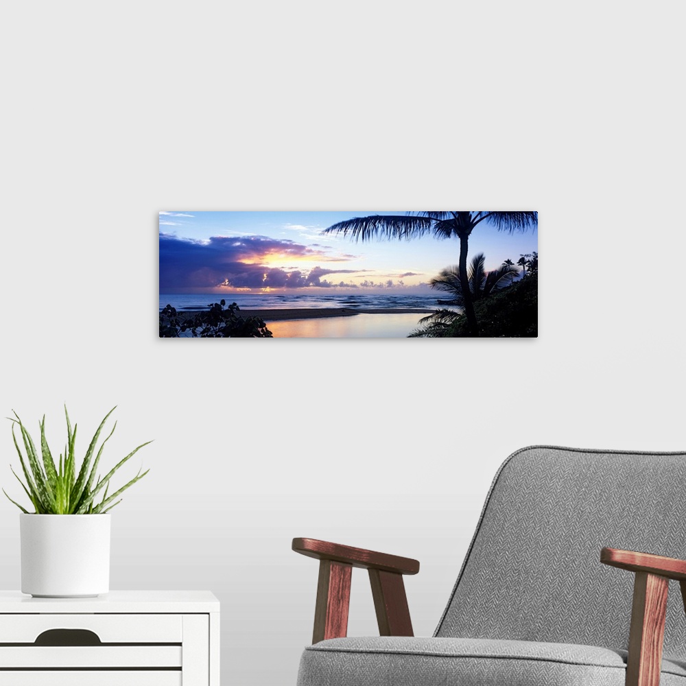 A modern room featuring Clouds filled the horizon as the sun sets behind them and in the foreground silhouetted tropical ...