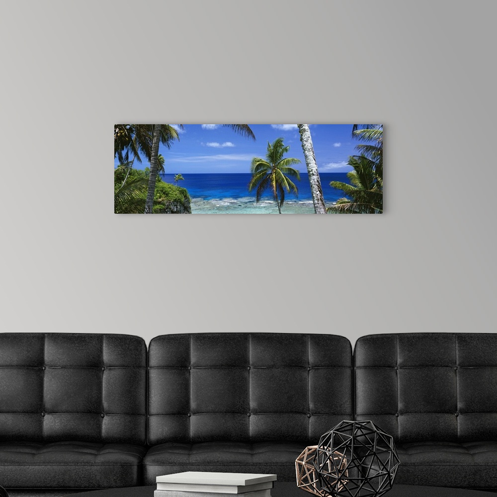 A modern room featuring Giant, panoramic photograph of palm trees on the beach of Nive Island, in front of the deep blue ...