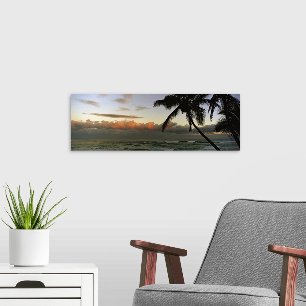 A modern room featuring Late afternoon photograph of a tropical seascape with silhouetted palm trees and rolling stormy c...