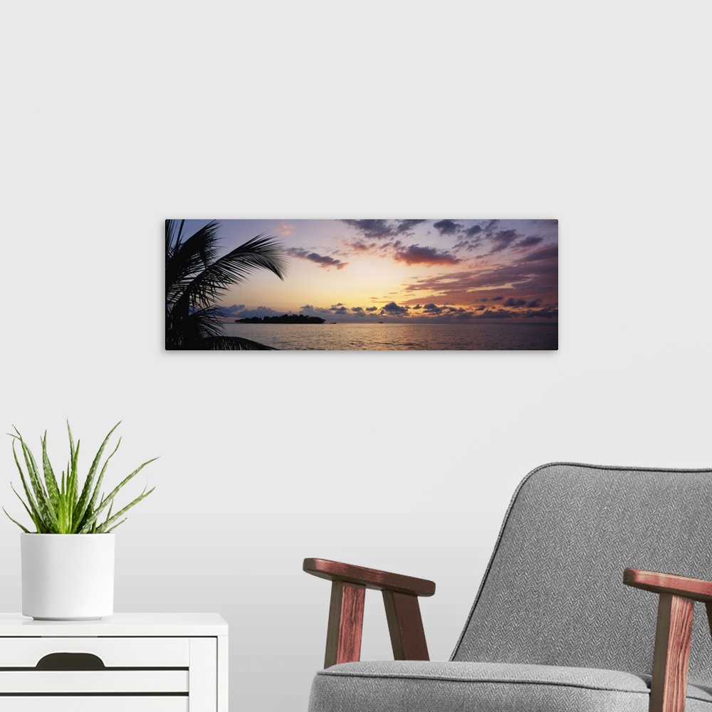 A modern room featuring Wide angle photograph of a cloudy ocean sunset with the silhouette of a palm tree in the foregrou...