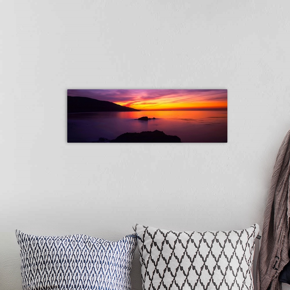 A bohemian room featuring A beautiful sunset photograph with warm tones in the sky that reflect in the ocean.