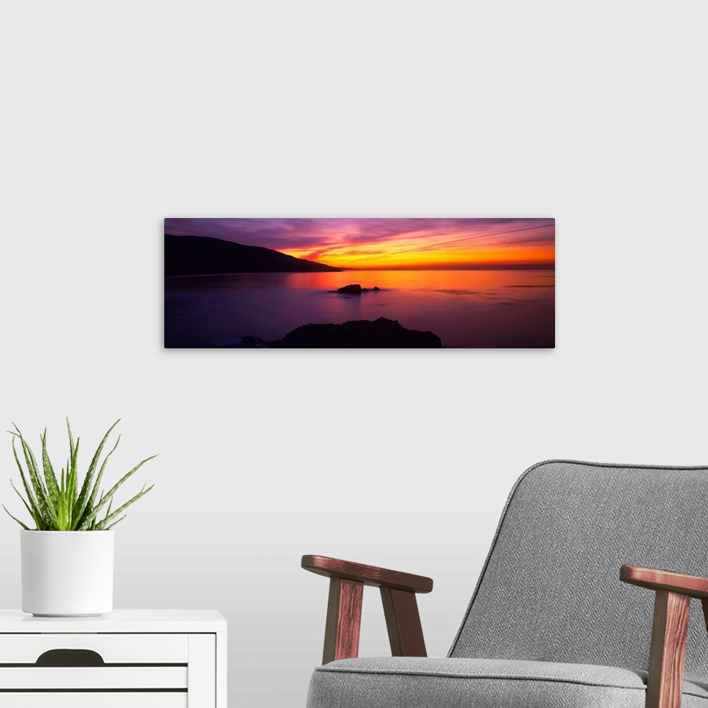 A modern room featuring A beautiful sunset photograph with warm tones in the sky that reflect in the ocean.