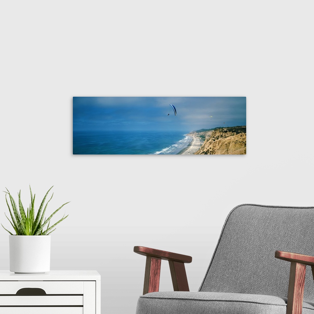 A modern room featuring Horizontal photograph on a giant canvas of several paragliders floating over bright blue waters a...