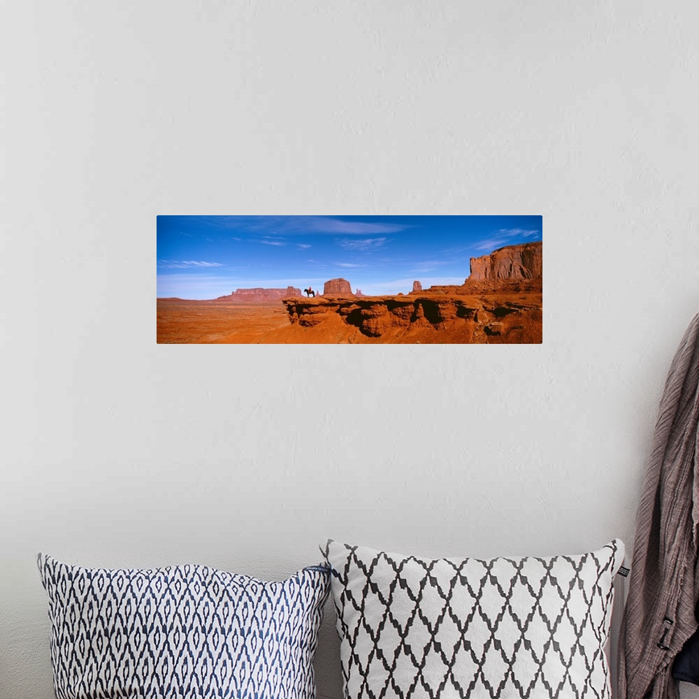 A bohemian room featuring A man on a horse at the edge of a cliff overlooking the arid desert of Monument Valley on a clear...