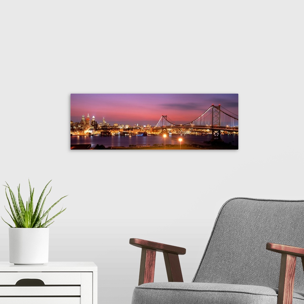 A modern room featuring Oversized panoramic artwork of a night time photograph of the Benjamin Franklin Bridge leading to...