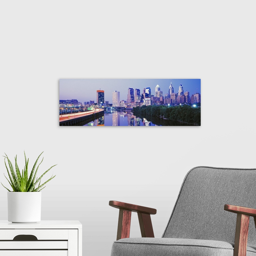 A modern room featuring This artwork is a panoramic canvas of the city skyline reflecting in the river water at dusk.