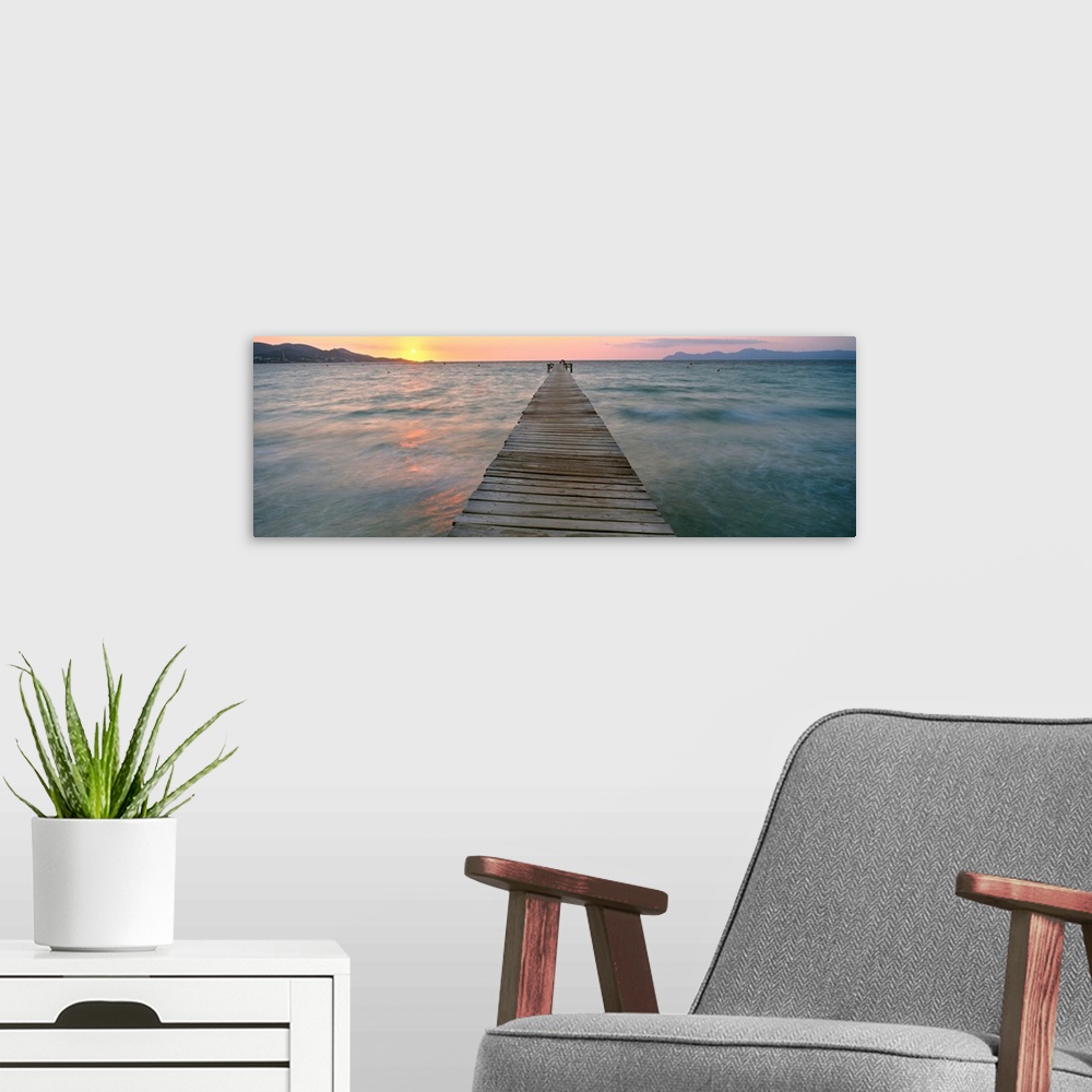 A modern room featuring Panoramic photograph of wooden dock stretching into ocean at dusk with mountain silhouettes in th...