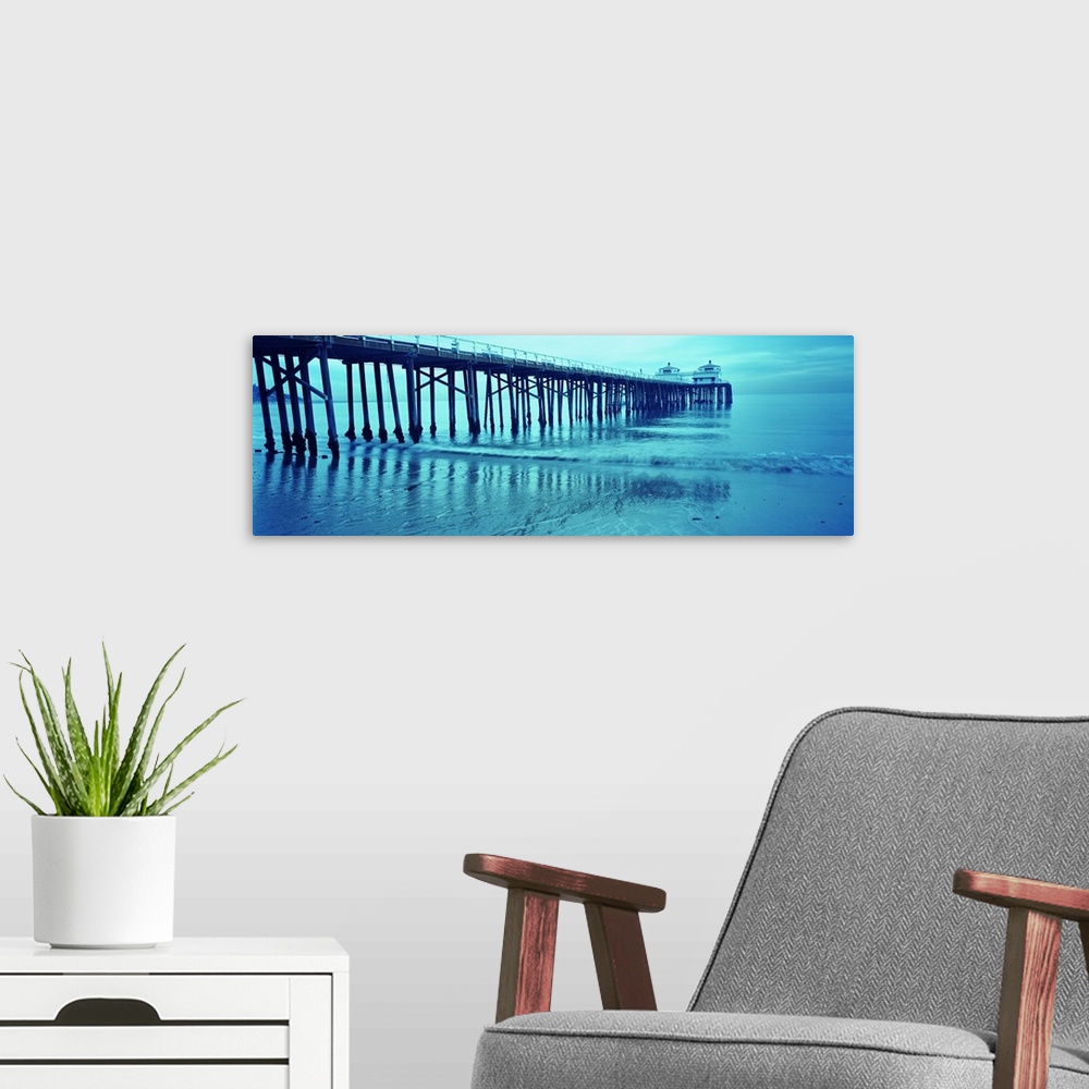 A modern room featuring Monotone photograph of a long pier reaching out into the Pacific Ocean at dusk with shallow waves...