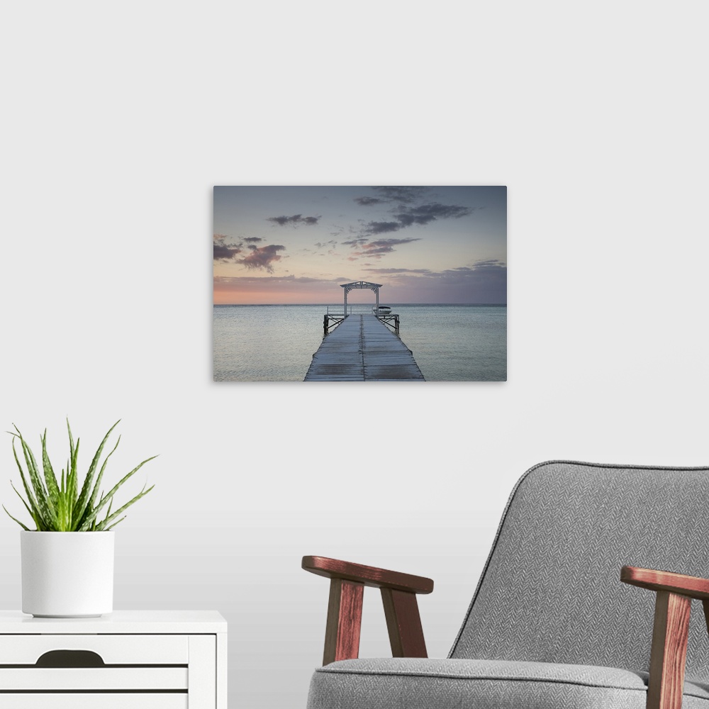 A modern room featuring Photograph of wooden dock stretching into ocean at sunset under a cloudy sky.