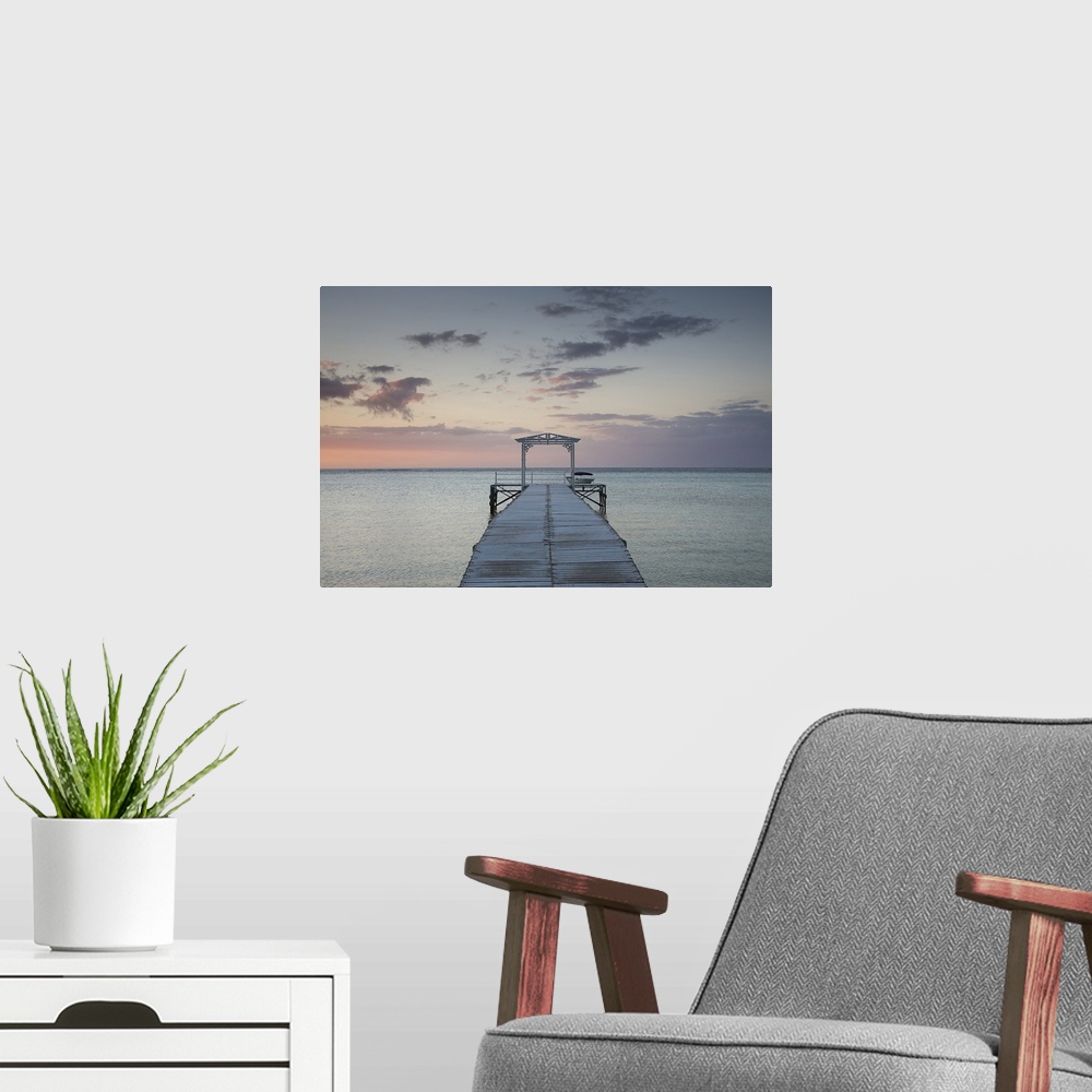 A modern room featuring Photograph of wooden dock stretching into ocean at sunset under a cloudy sky.