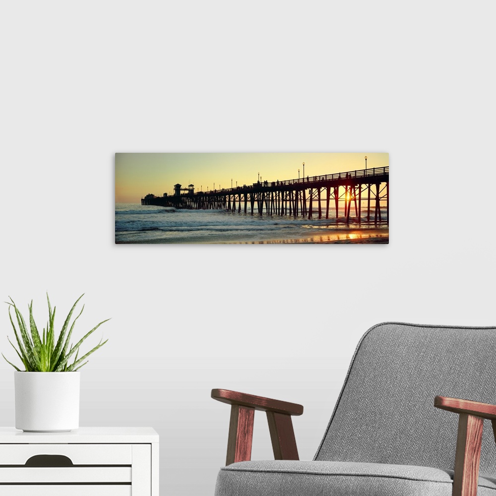 A modern room featuring Panoramic wall docor of the silhouette of a pier reaching into the ocean surf at sunset.