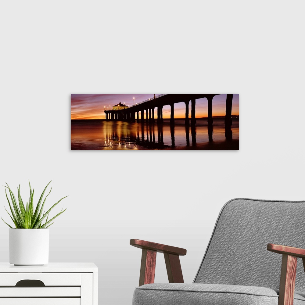 A modern room featuring A panoramic photograph of the silhouette of a long pier over the ocean at sunset.